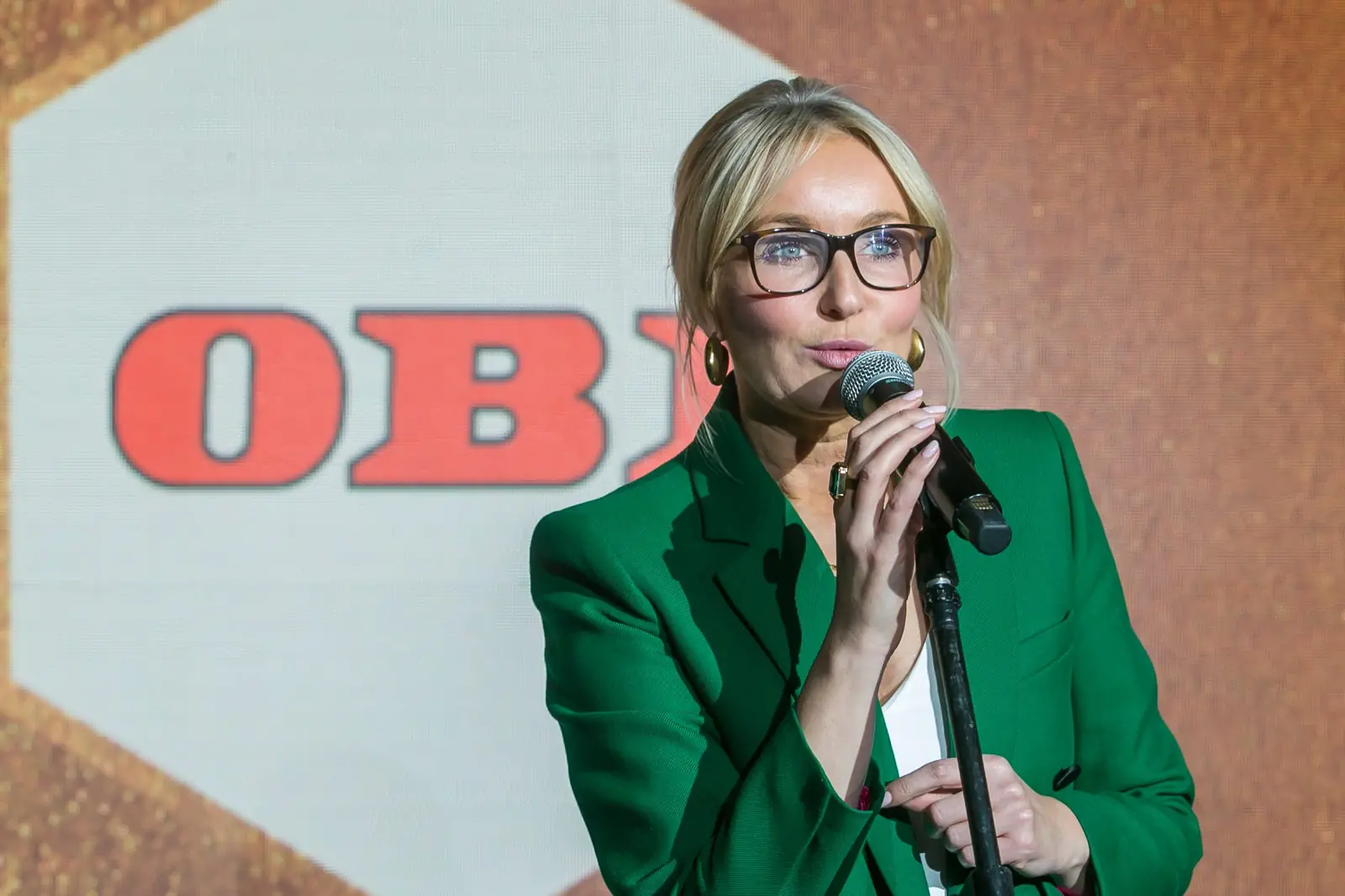 Laureatka w okularach i zielonym żakiecie przemawia przy mikrofonie na tle czerwonego logo — Gala DMR XI (2022)