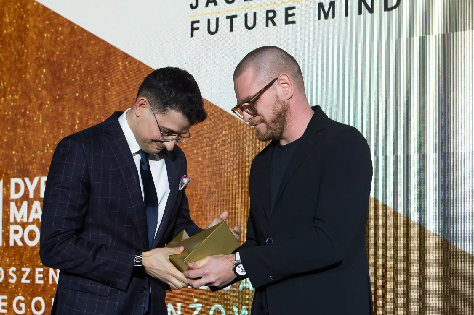 Laureat w granatowym garniturze w kratę przejmuje statuetkę, obaj mężczyźni patrzą na nagrodę — Gala DMR XI (2022)