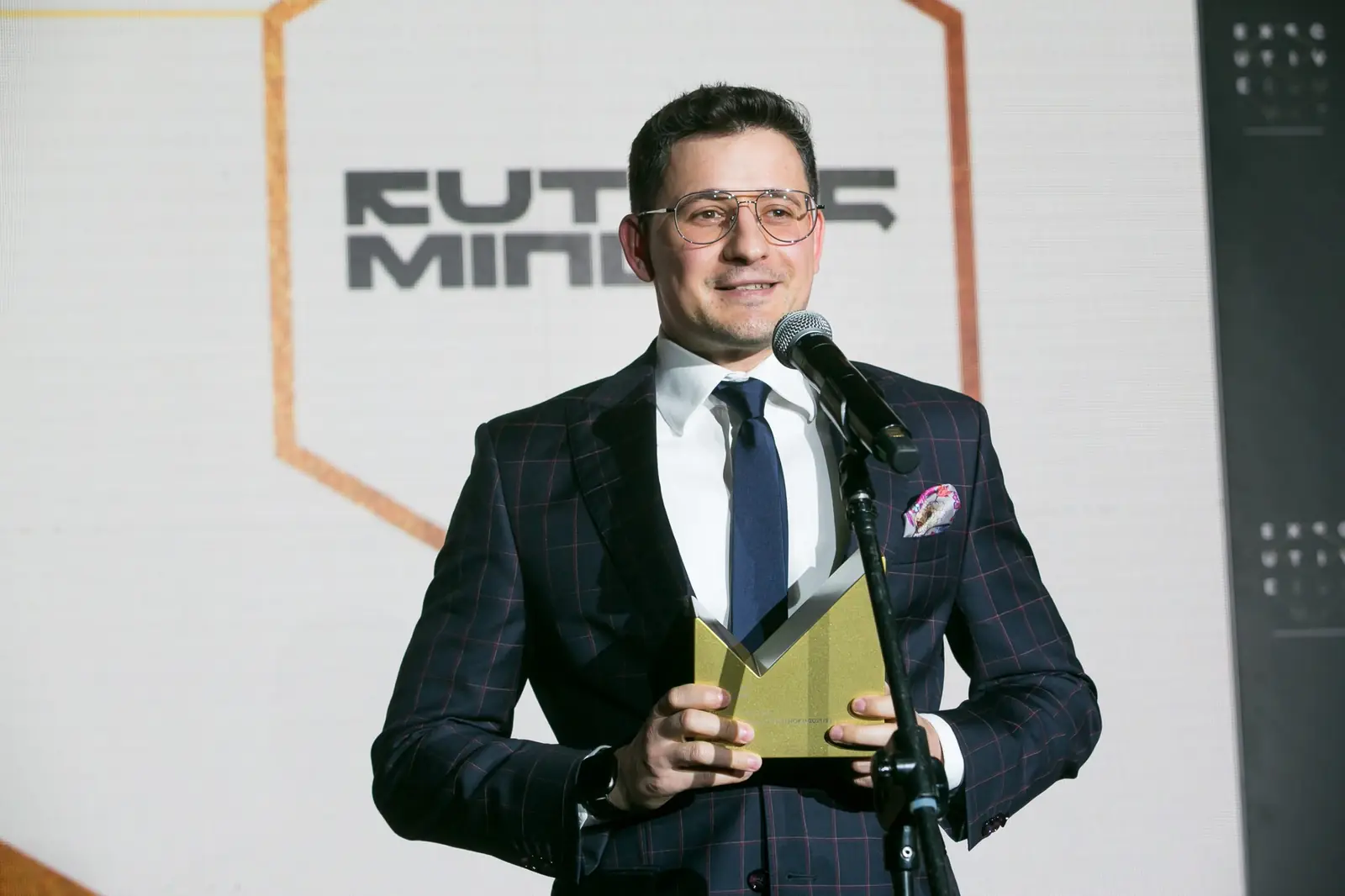 Uśmiechnięty laureat z poszetką stoi przy mikrofonie, trzymając statuetkę oburącz — Gala DMR XI (2022)