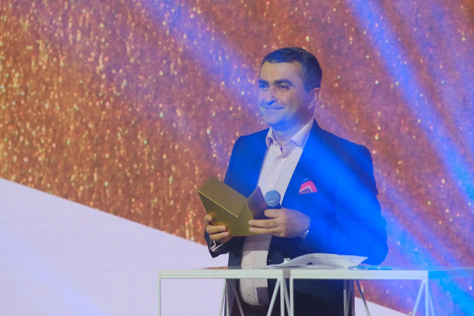 Laureat w granatowym garniturze uśmiecha się przy mównicy, trzymając złotą statuetkę — Gala DMR XII (2023)