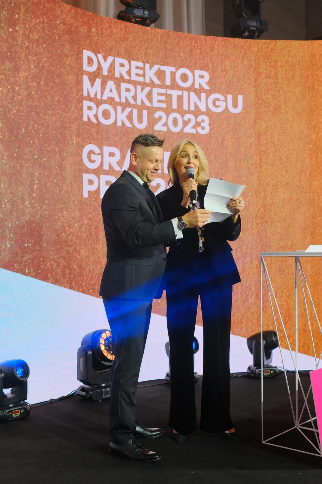 Prowadzący w smokingu i prowadząca w czerni czytają z karty werdykt Grand Prix — Gala DMR XII (2023)
