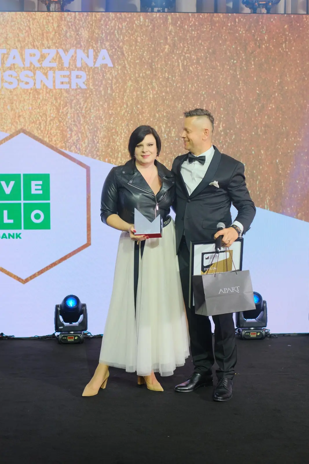 Winner in a light skirt holds a statuette beside the host with a diploma on the Grand Prix stage — DMR Gala XII (2023)