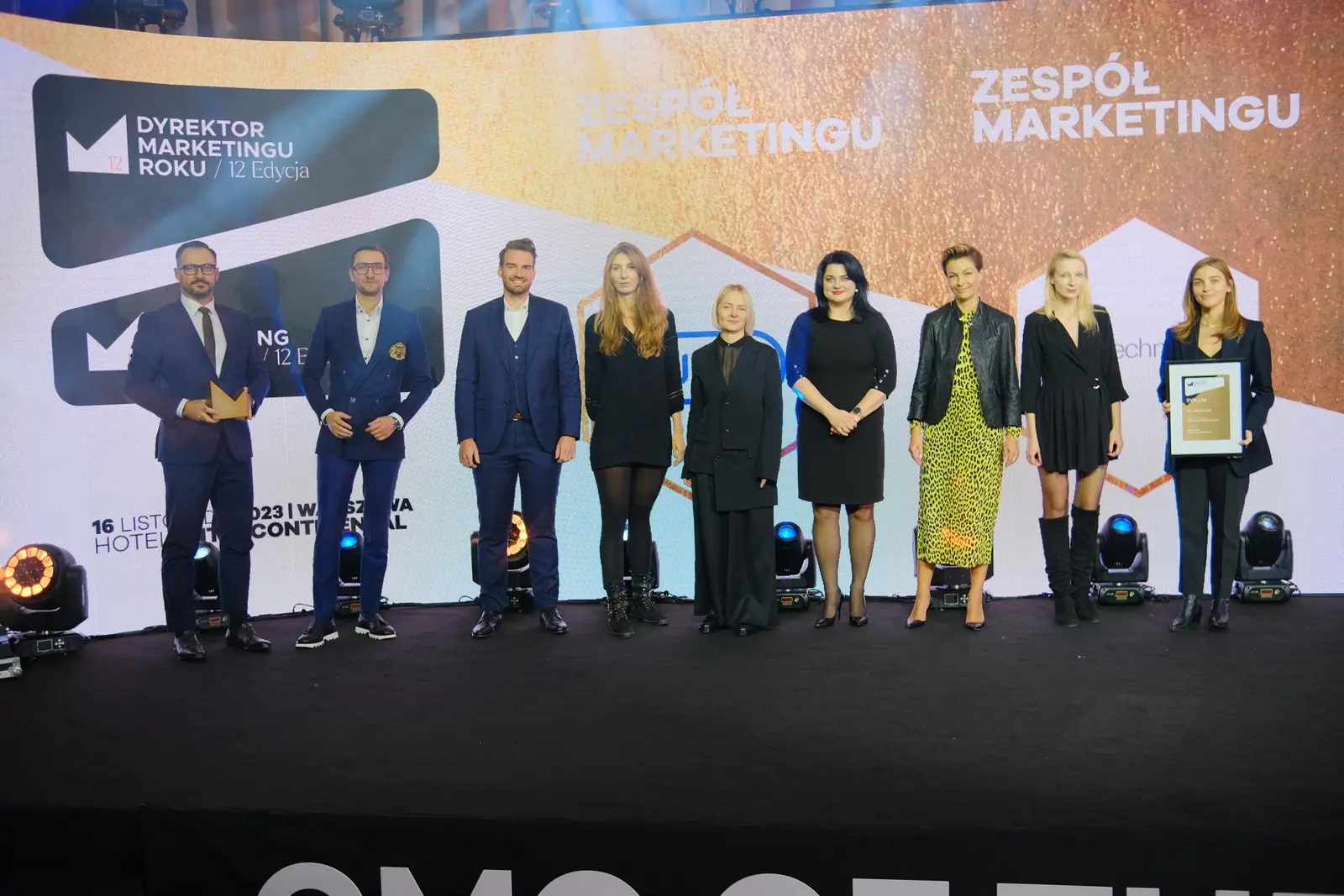 Dziewięć osób z nagrodzonego zespołu marketingu stoi w szeregu na scenie z logo konkursu — Gala DMR XII (2023)