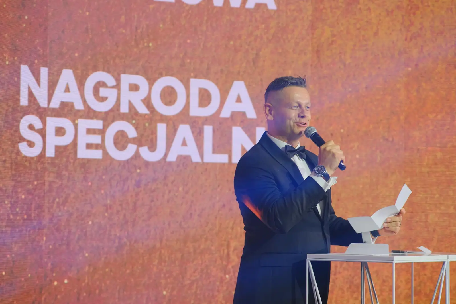 Prowadzący zapowiada Nagrodę Specjalną, czytając do mikrofonu z trzymanej kartki — Gala DMR XII (2023)