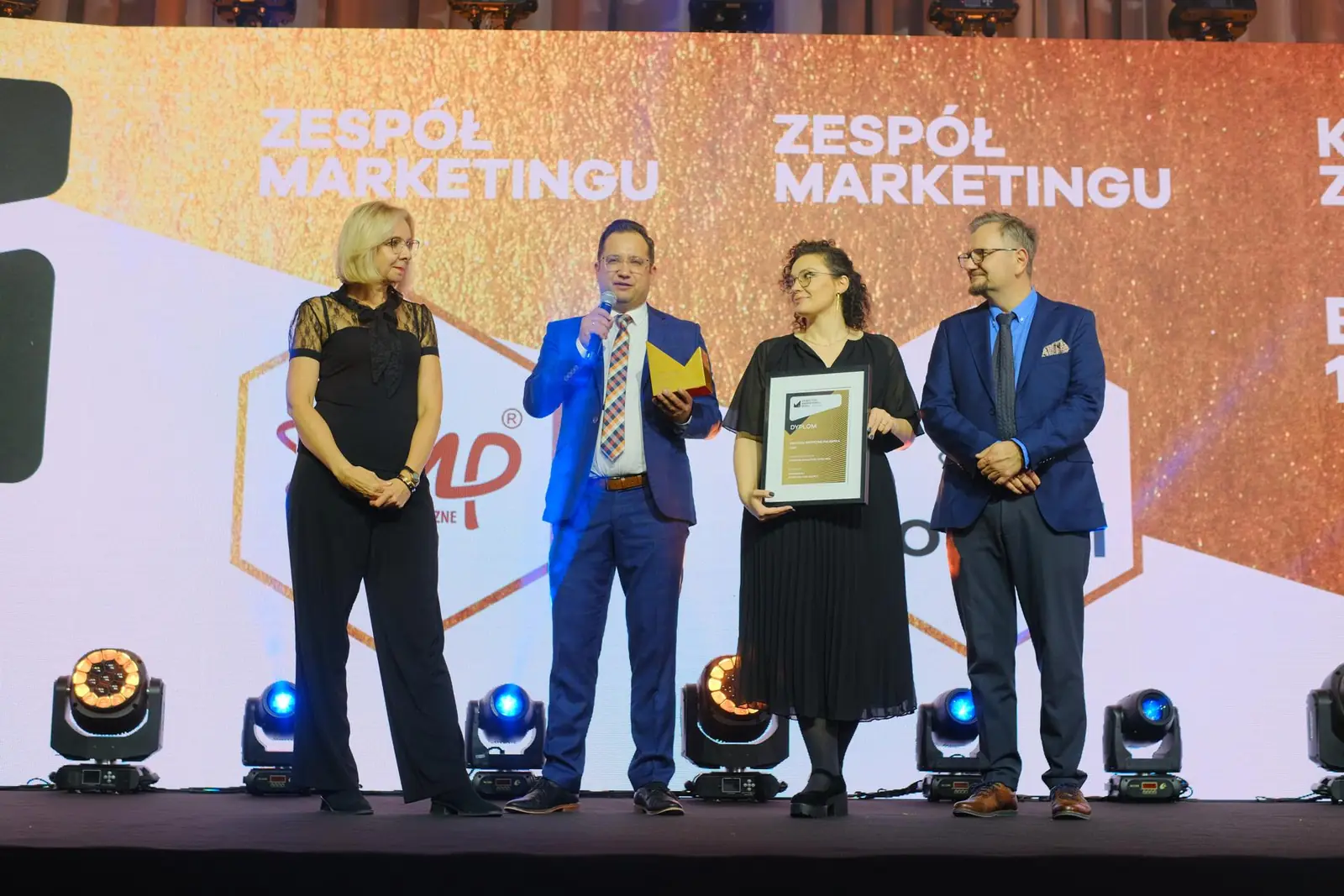 Czworo osób na scenie pozuje z dyplomem i statuetką w kategorii Zespół Marketingu — Gala DMR XII (2023)