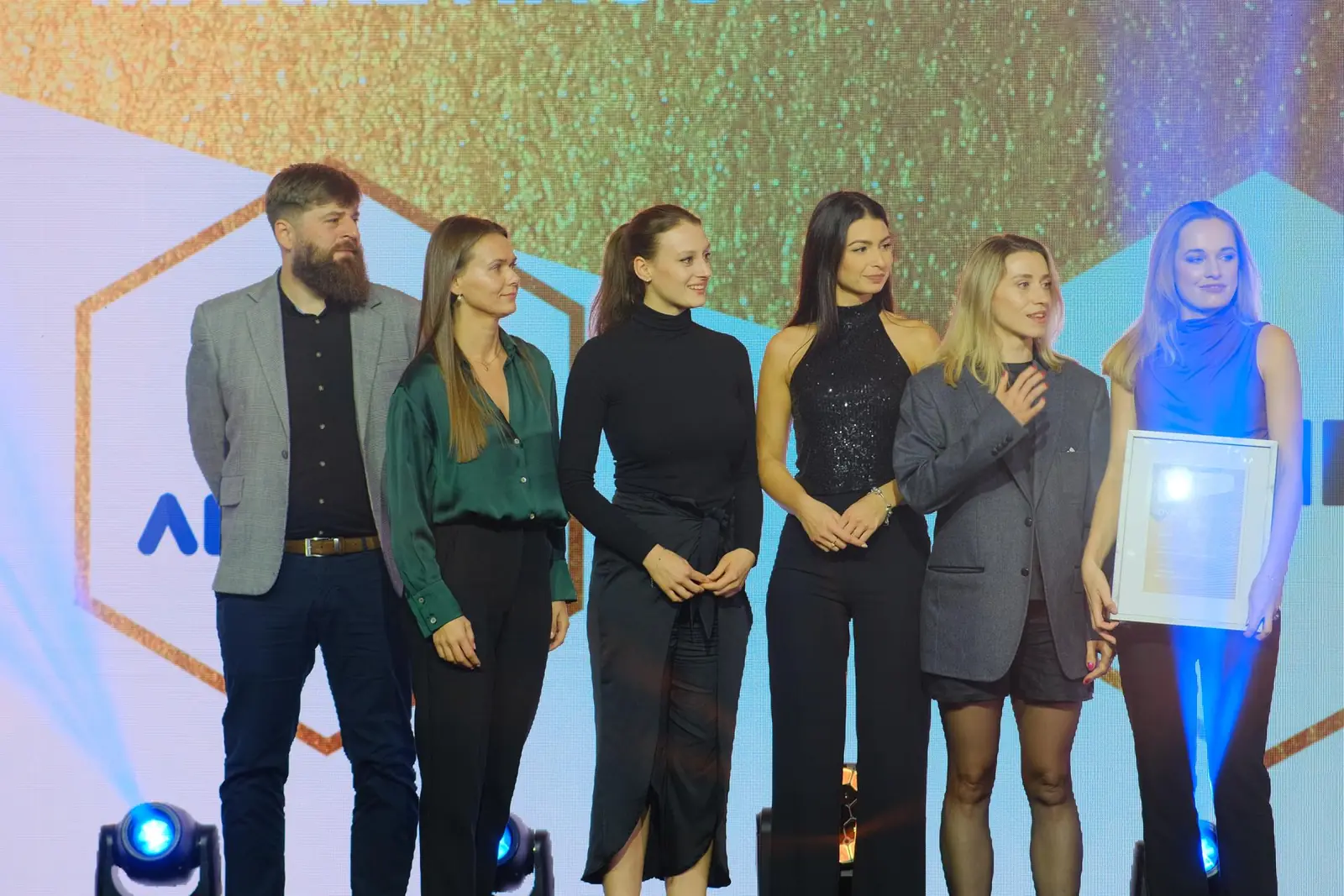 Six-person team with a framed diploma stands on stage in blue spotlight glow — DMR Gala XII (2023)