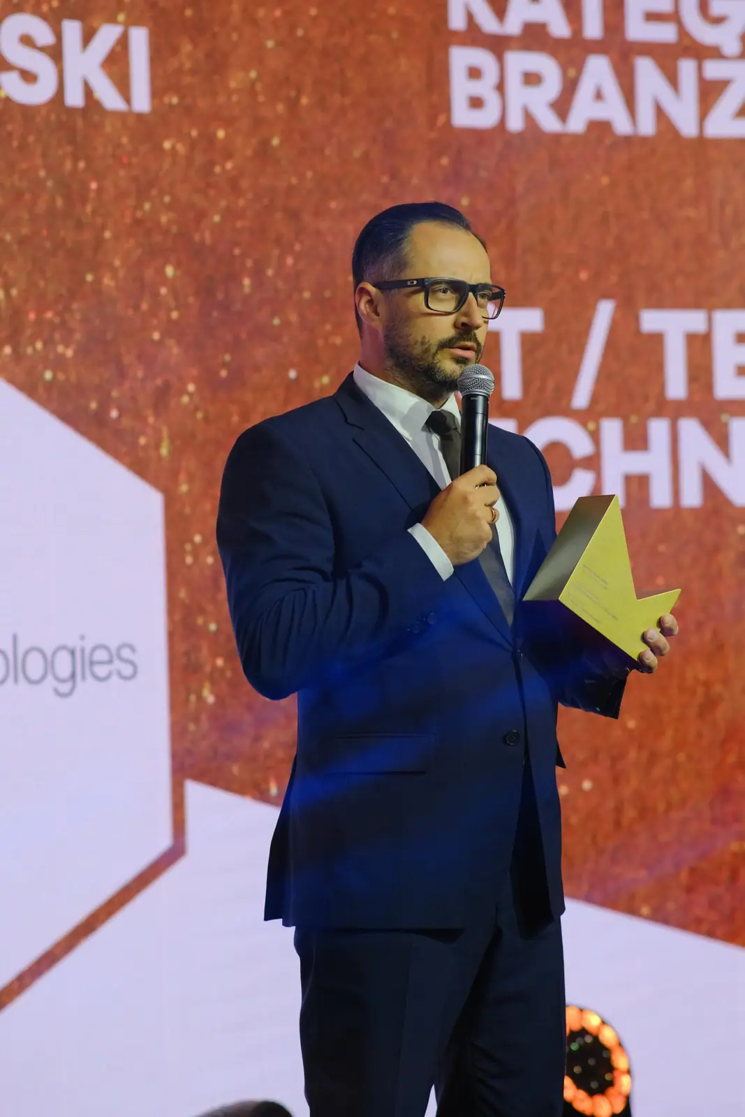 Laureat z brodą przemawia ze statuetką w dłoni w kategorii branżowej IT i technologie — Gala DMR XII (2023)
