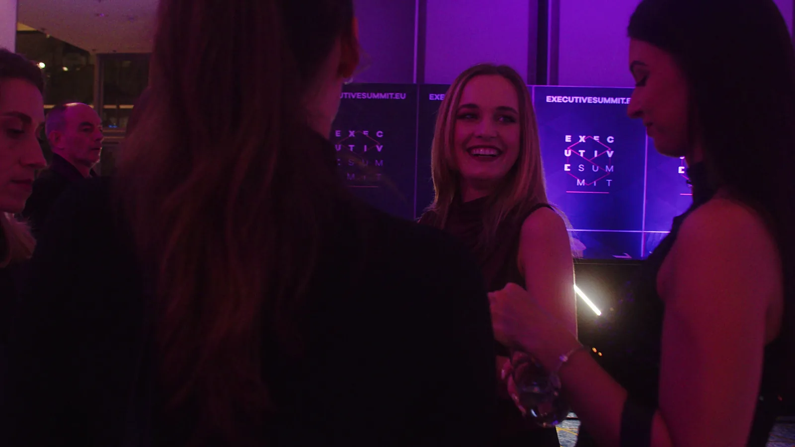 Smiling blonde woman chats with guests in the purple light of the networking area — DMR Gala XII (2023)