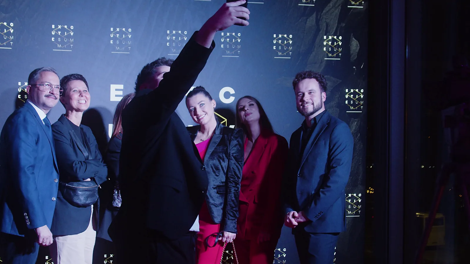 Grupa gości pozuje do wspólnego selfie przed ścianką z logotypami wydarzenia — Gala DMR XII (2023)