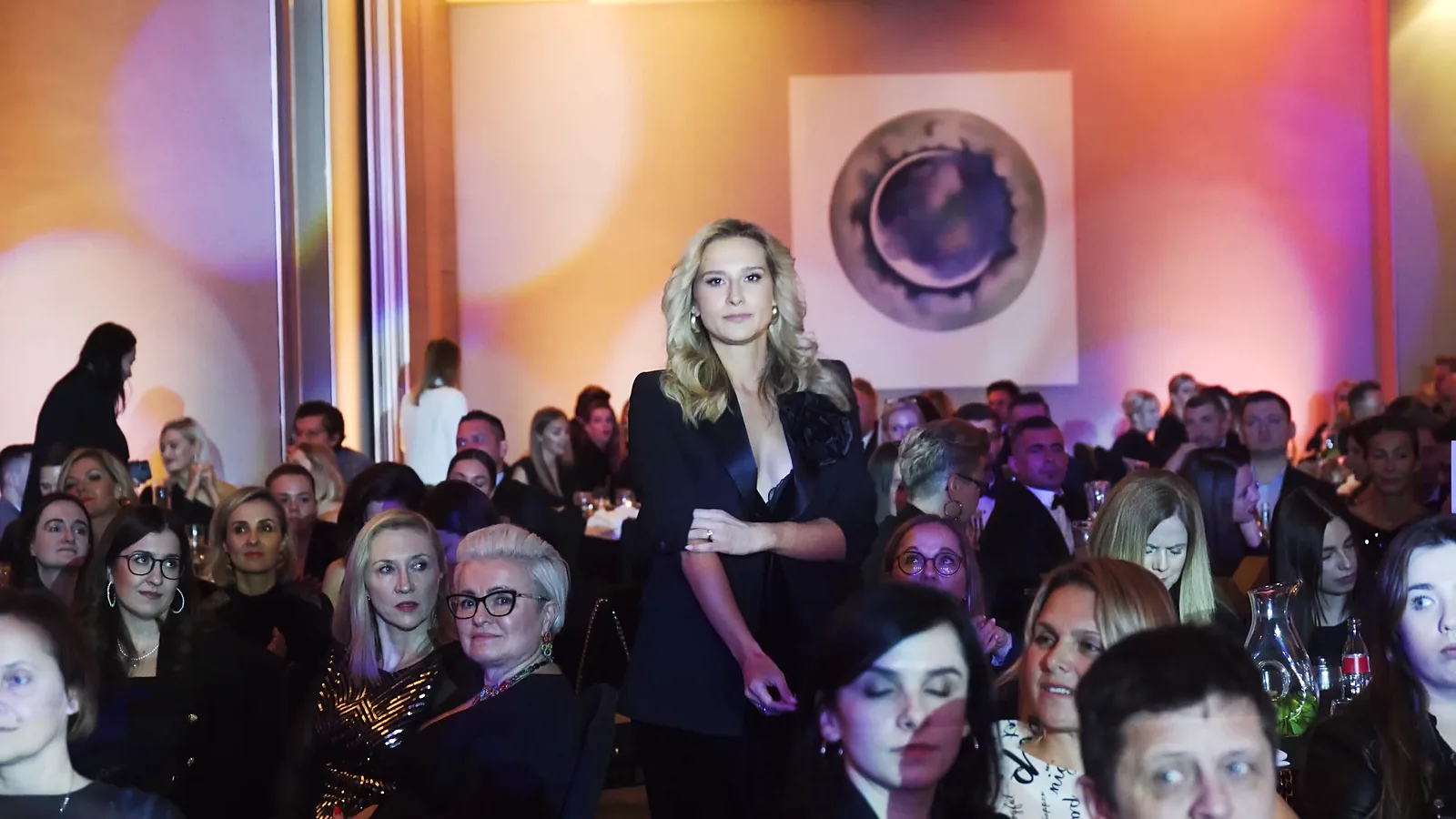 Blondynka w czarnym stroju stoi wśród siedzącej publiczności w wypełnionej sali balowej — Gala DMR XII (2023)