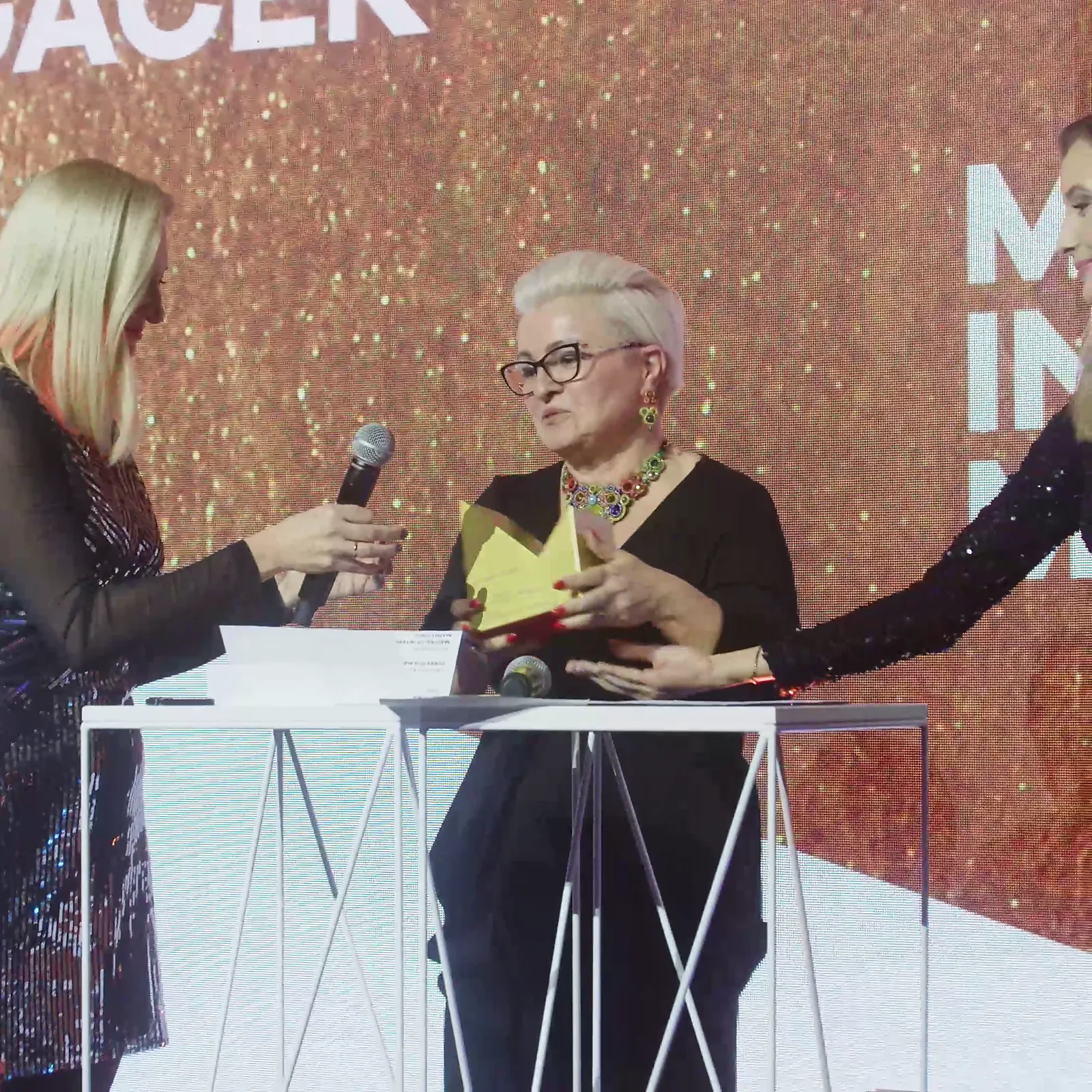 Laureatka z krótkimi siwymi włosami przemawia przy mównicy, a prowadząca podaje jej mikrofon — Gala DMR XII (2023)