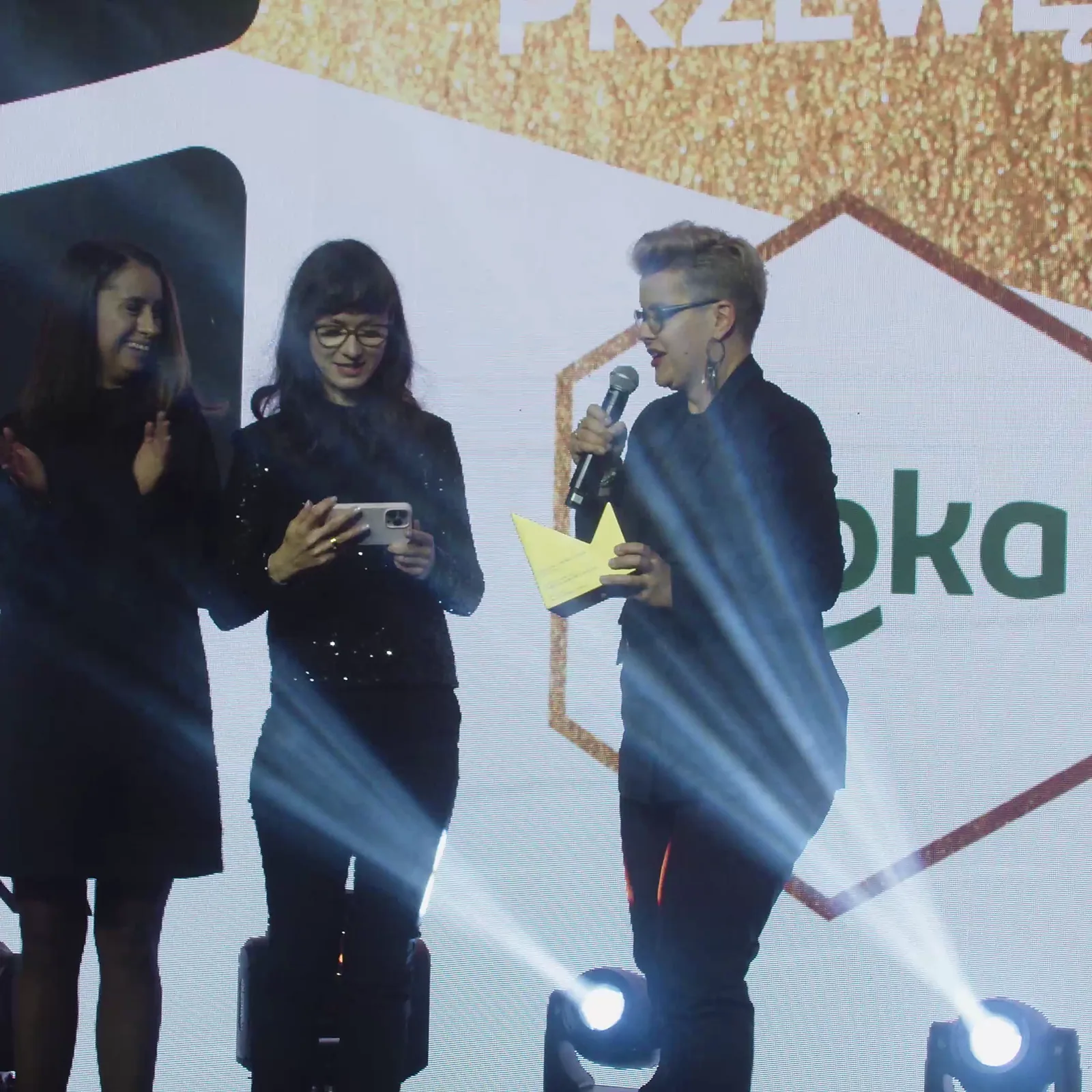 Laureatka z krótkimi jasnymi włosami przemawia ze statuetką, jedna z koleżanek bije jej brawo — Gala DMR XII (2023)