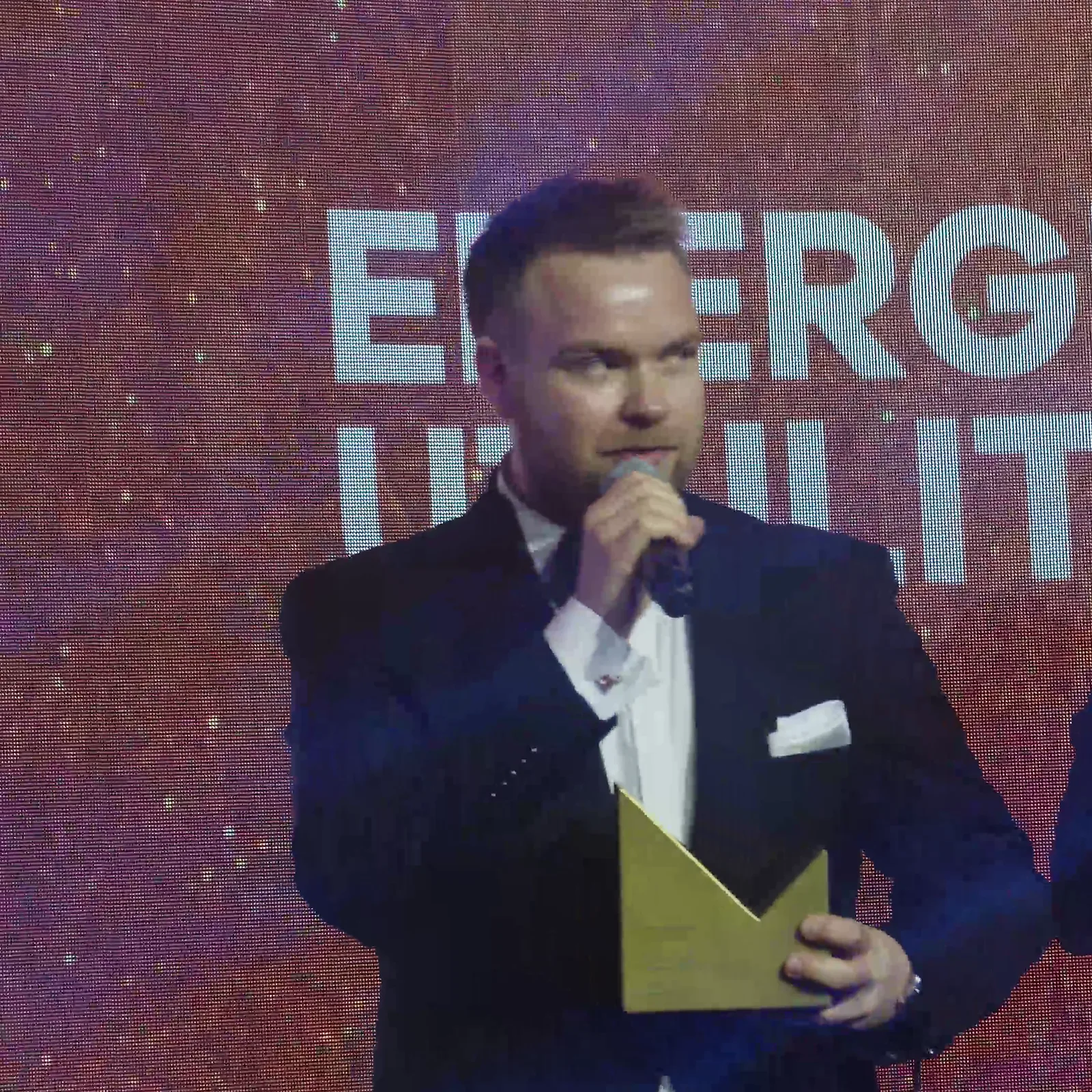 Laureat z jasnymi włosami i poszetką przemawia ze statuetką w kategorii energetycznej — Gala DMR XII (2023)