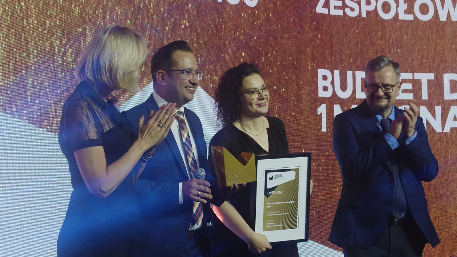 Laureatka z kręconymi włosami i dyplomem uśmiecha się, a wręczający biją brawo — Gala DMR XII (2023)