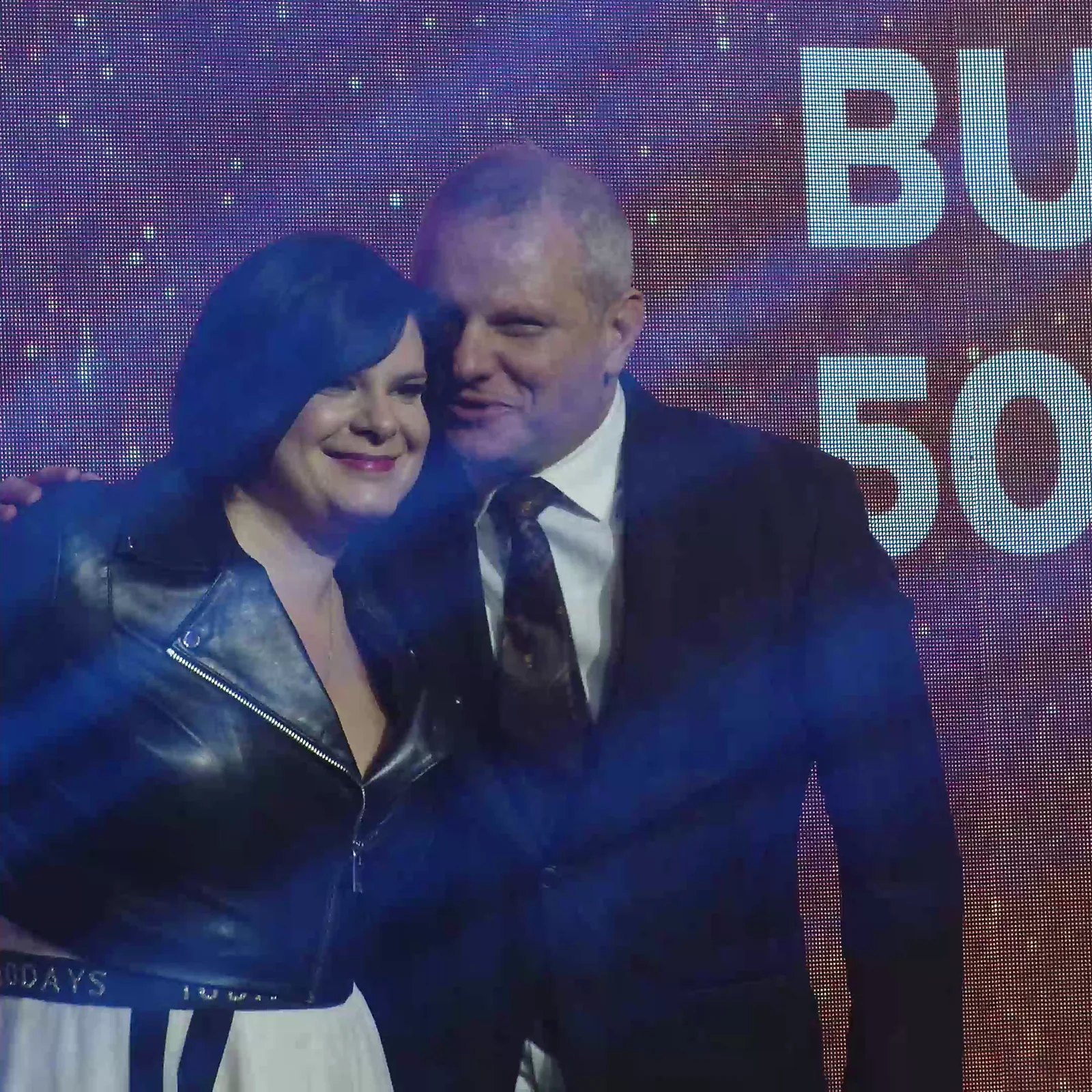 Laureatka w skórzanej kurtce przytula się do mężczyzny w garniturze w niebieskim świetle — Gala DMR XII (2023)