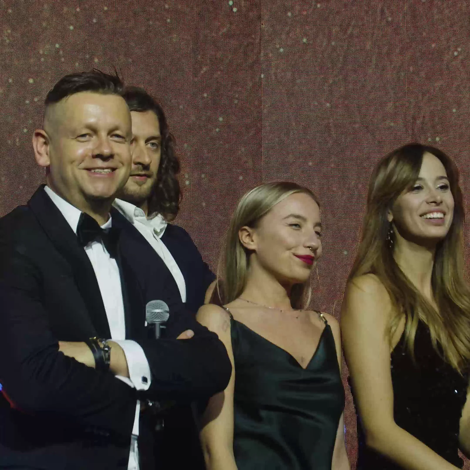 Zbliżenie: uśmiechnięty prowadzący ze skrzyżowanymi rękami w towarzystwie trzech gości — Gala DMR XII (2023)