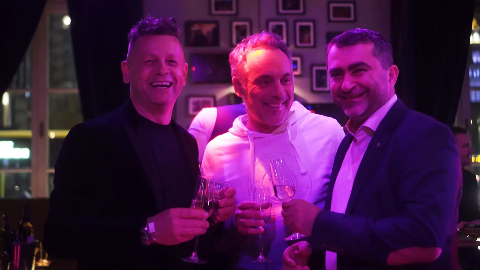 Trzech roześmianych mężczyzn wznosi toast kieliszkami wina w fioletowym świetle after party — Gala DMR XII (2023)