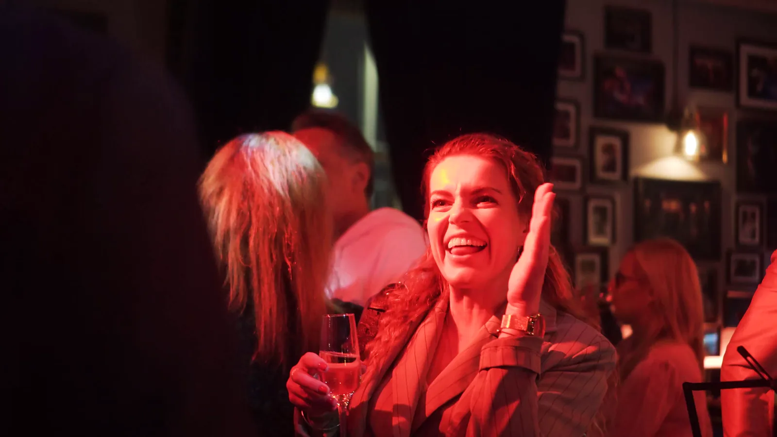 Kobieta w czerwonym świetle śmieje się i klaszcze z kieliszkiem w dłoni na after party — Gala DMR XII (2023)